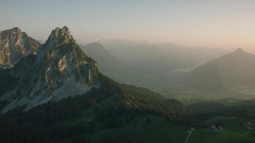 A majestic static view of the Swiss Alps at sunrise, overlooking a misty valley and rolling green hills