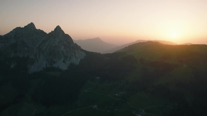 Static aerial shot of a stunning mountain valley with sharp peaks and rolling green hills during a peaceful sunrise