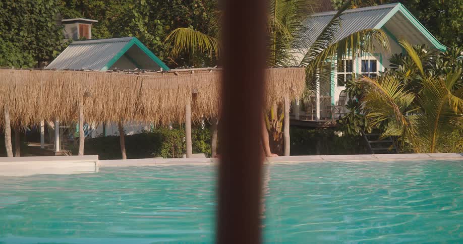 A relaxed woman in a swimsuit enjoys the sun while sitting on the edge of a beautiful resort swimming pool