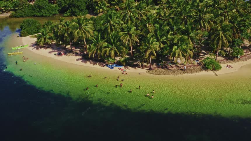 Aerial drone footage zooms in on an idyllic tropical island paradise where people swim and relax in the vibrant turquoise water