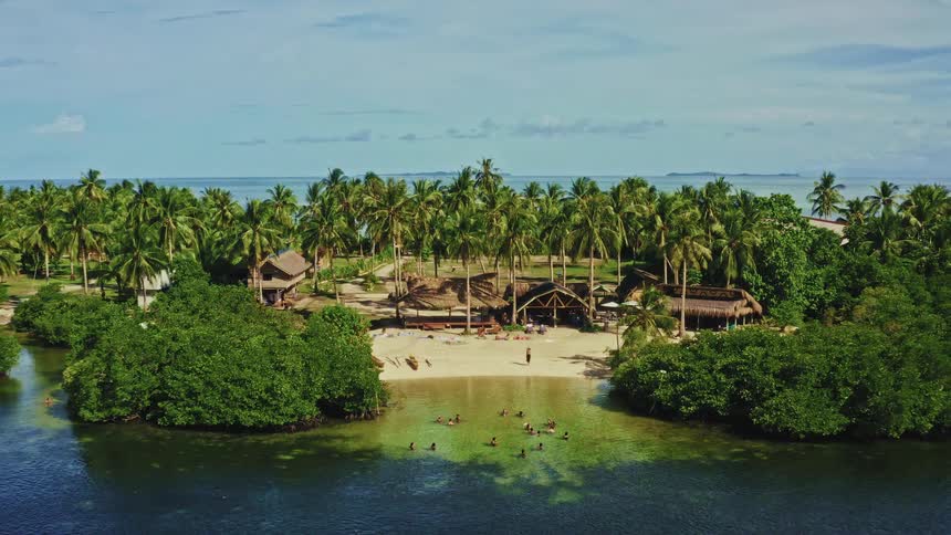 An aerial view reveals a stunning tropical paradise resort, with tourists sunbathing on the beach and swimming in the calm, clear waters of a hidden cove