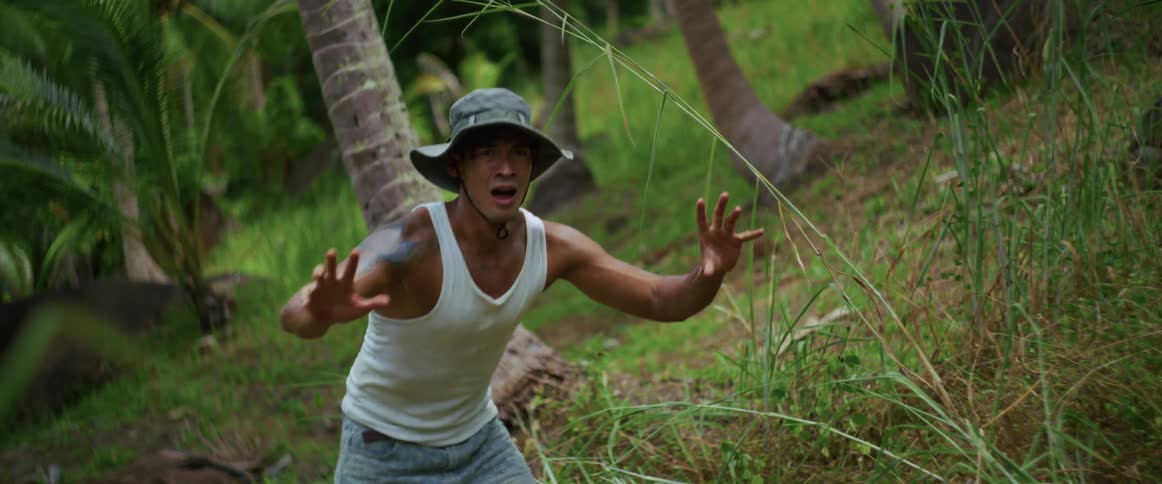 A man in a bucket hat freezes with a terrified expression on his face while in a dense, green tropical jungle
