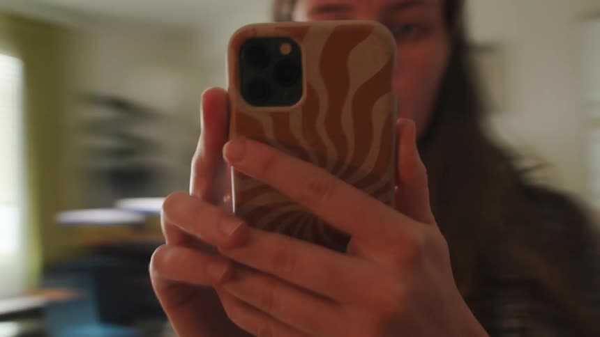 Close-up point of view shot of a woman walking through her apartment while filming a mirror selfie video