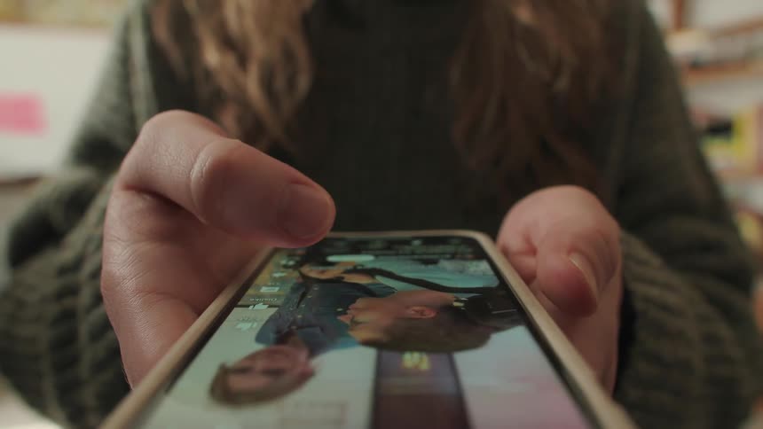 A close-up shot of a person's hands as they scroll through a social media feed on their smartphone