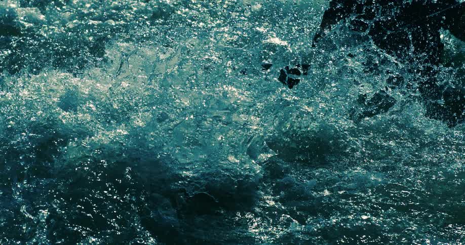 Super slow-motion close-up of turbulent blue-green water splashing against a raft in a powerful river