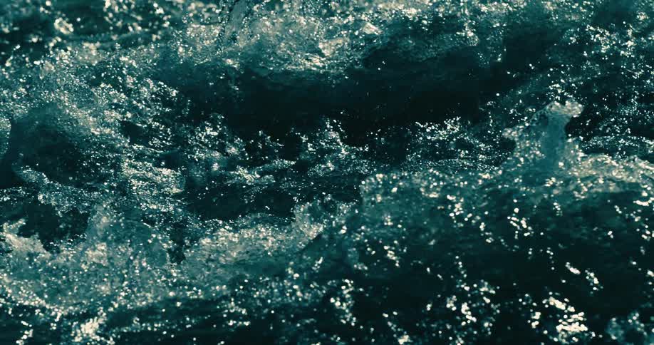 Powerful currents of dark teal water churn and bubble in a dramatic slow motion close-up
