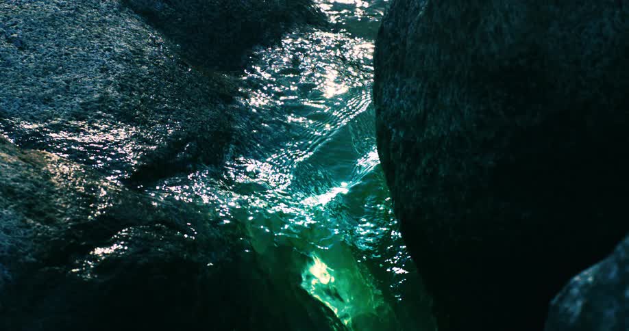 A serene slow motion close up of sparkling turquoise water flowing between dark rocks