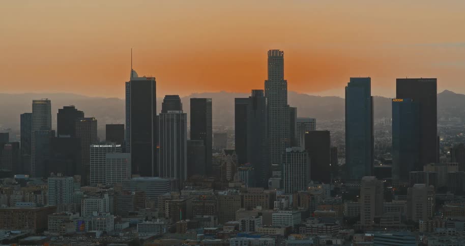 A slow zoom out reveals the downtown Los Angeles skyline and its towering skyscrapers against a beautiful orange sunset