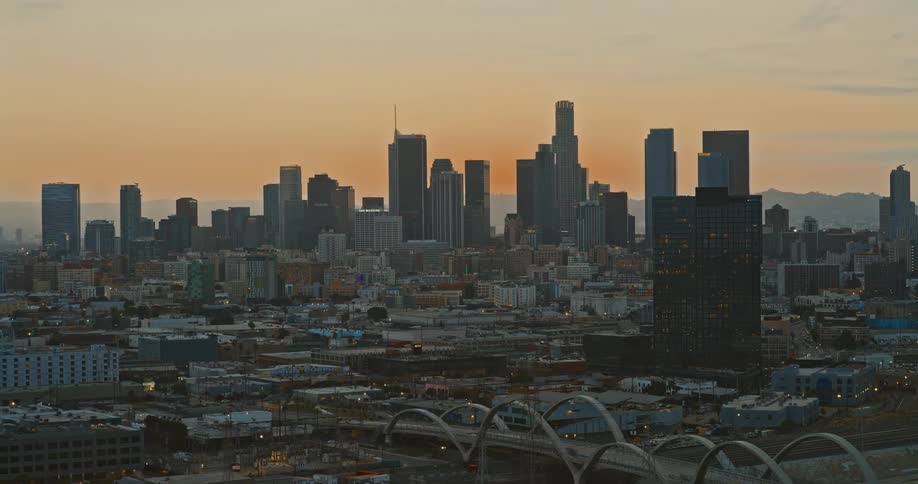 An aerial shot slowly pushes in on the Downtown Los Angeles skyline with the 6th Street Viaduct in the foreground during a warm sunrise