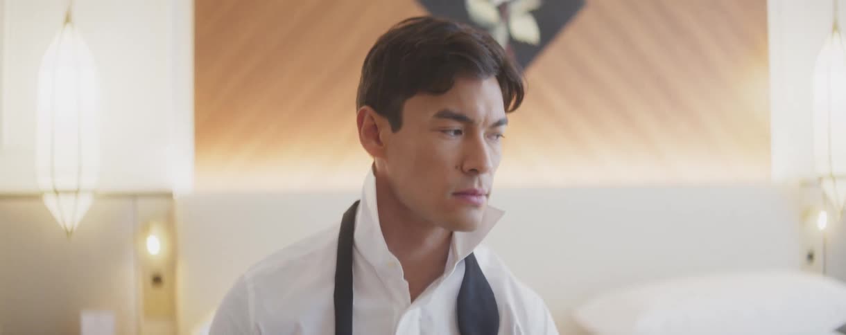 A handsome young man sits thoughtfully in a bright bedroom, preparing to tie his bow tie for a formal event