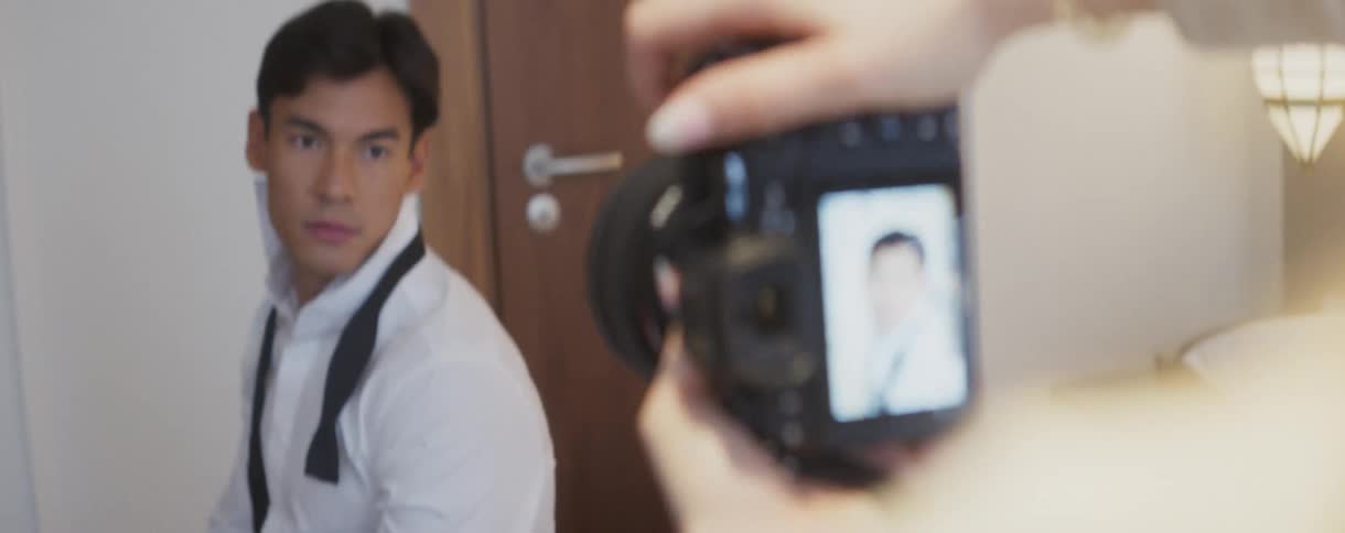 Over-the-shoulder shot of a photographer taking a portrait of a male model, with the camera's screen in focus