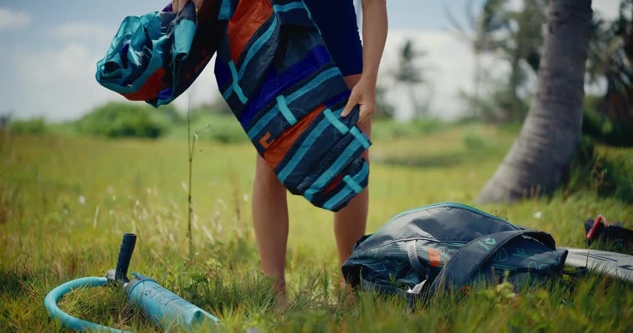 Slow motion shot of a woman unrolling her colorful kite in a grassy field to prepare for a kitesurfing session