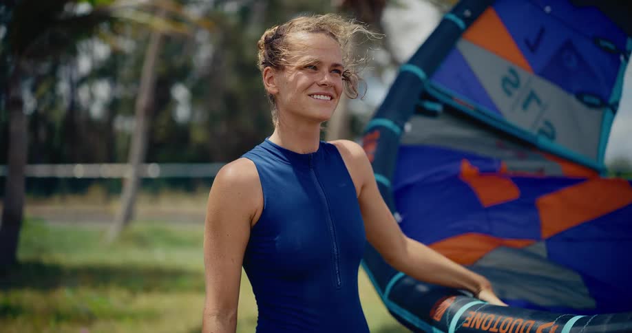 Slow motion shot of a beautiful smiling woman in a wetsuit holding her kitesurfing kite in a windy, tropical location