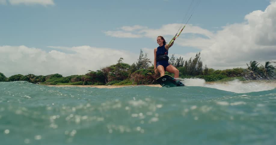 A woman kitesurfing in slow motion glides past the camera in the turquoise ocean on a beautiful sunny day