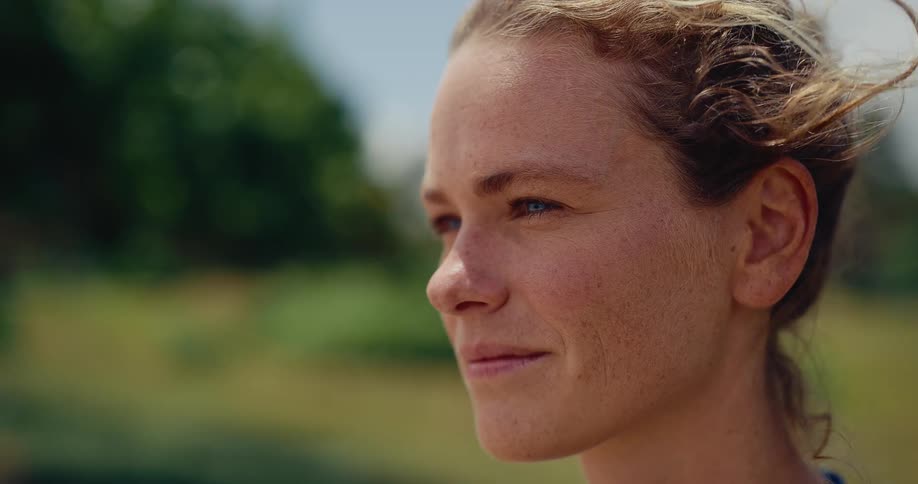 A beautiful slow-motion close-up of a happy, freckled woman smiling as the wind blows through her curly hair