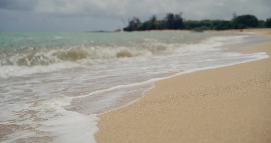 A relaxing close-up shot of gentle ocean waves washing onto a sandy beach in slow motion
