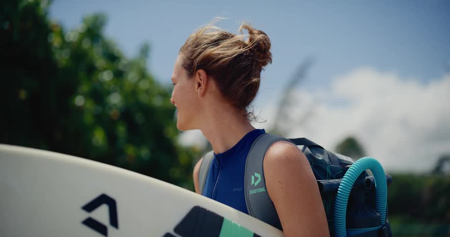Slow motion close-up of a smiling female kitesurfer holding her board, ready for an ocean adventure on a windy tropical day