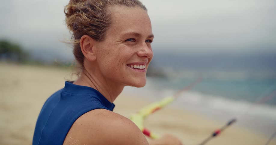 Portrait of an athletic woman in a wetsuit on a sandy beach smiling as she looks out at the ocean waves
