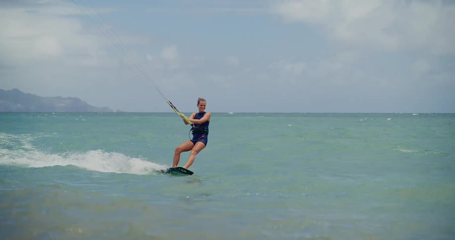 An athletic woman expertly kitesurfs across the ocean, captured in a stunning slow-motion shot
