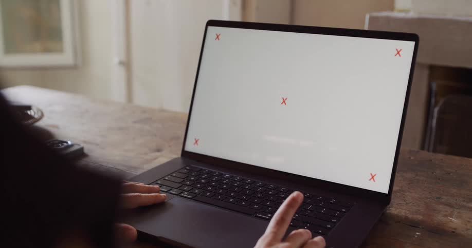 An over-the-shoulder shot of a person working on a laptop with a blank screen sitting at a rustic wooden table