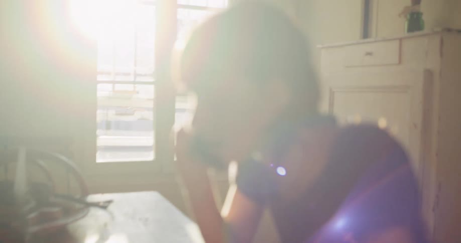 Intimate handheld footage captures a young woman on a phone call while working on her laptop in a sun-drenched apartment
