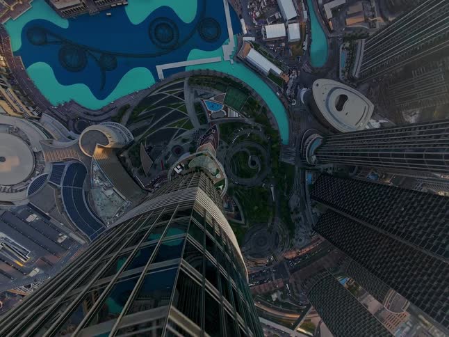 A dizzying top-down aerial view slowly pans up the side of a skyscraper, revealing the downtown Dubai cityscape below