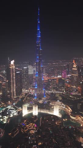 An aerial view of the Burj Khalifa and the surrounding Dubai skyline at night, showcasing a spectacular blue light show and the dancing Dubai Fountain