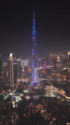 A stunning aerial view of the Burj Khalifa in Dubai, showcasing a brilliant blue light and fountain show against the vibrant city skyline at night
