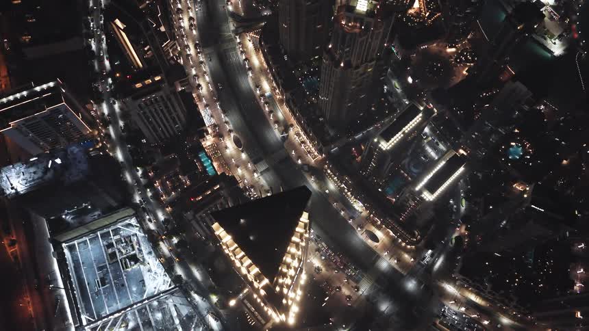 A stunning top-down aerial view of a bustling metropolis at night, with streams of traffic illuminating the streets between towering skyscrapers