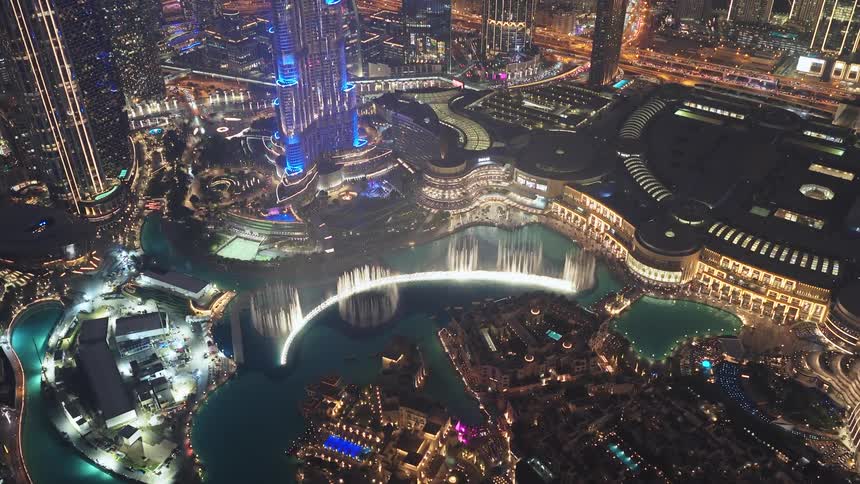 A stunning aerial view captures the spectacular Dubai Fountain show at night, with the iconic Burj Khalifa and the glowing cityscape in the background