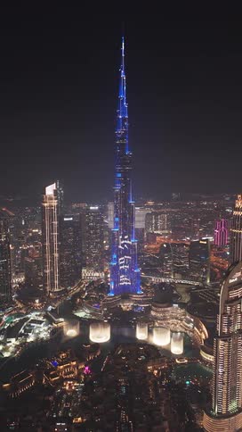 A stunning aerial view of the Burj Khalifa in Dubai at night, illuminated with a vibrant blue light show as the famous fountains dance below