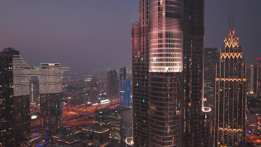 A stunning aerial view pulls back from the iconic Burj Khalifa, revealing the glittering Dubai skyline and sprawling city lights at dusk