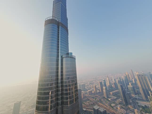 A breathtaking low-angle aerial shot slowly rises up the side of the majestic Burj Khalifa, revealing the vast Dubai cityscape below