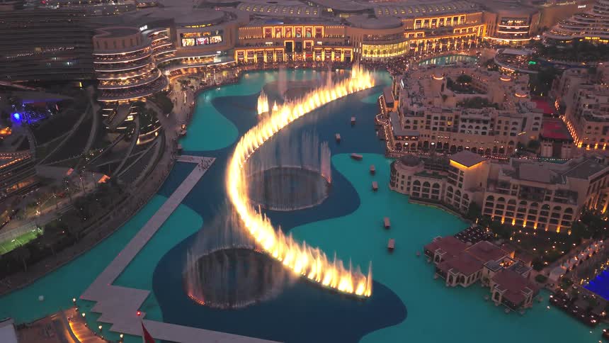 A stunning high-angle view of the Dubai Fountain's dazzling light and water show at night, surrounded by the glowing city skyline