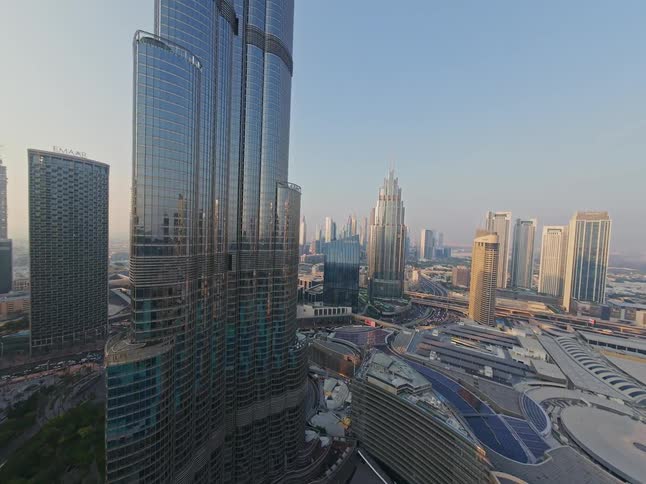 A stunning aerial push-in shot captures the iconic Burj Khalifa and the modern cityscape of downtown Dubai during a hazy sunset