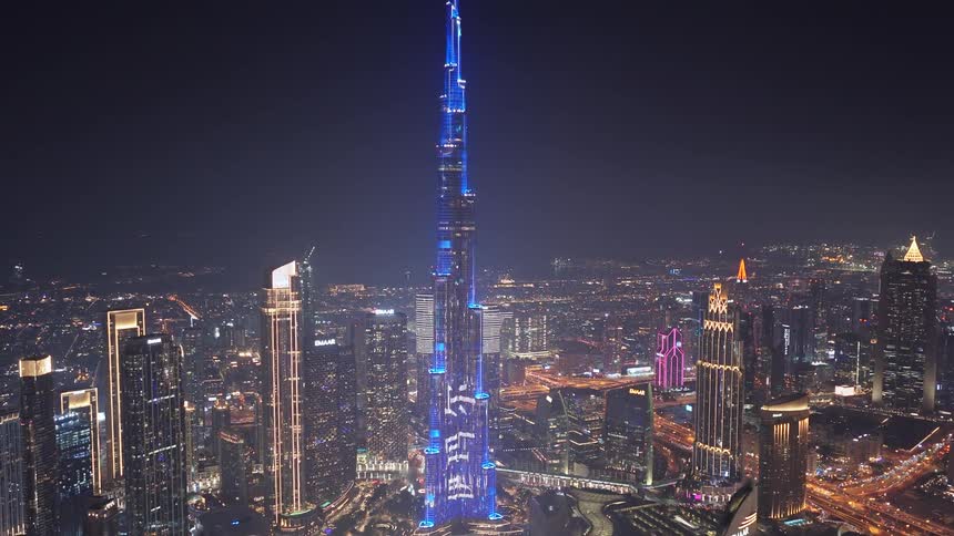 A stunning aerial view captures the Burj Khalifa's vibrant blue light show against the backdrop of the sprawling Dubai cityscape at night