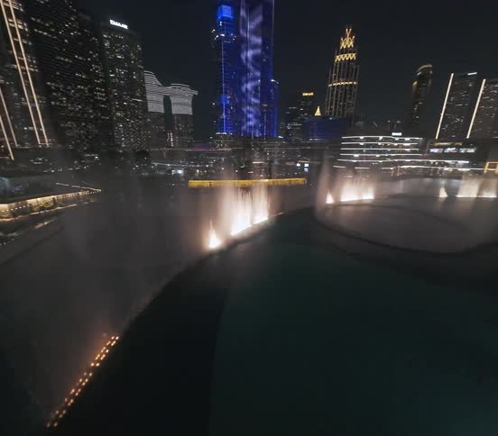 A spectacular aerial view of the Dubai Fountain show at night, culminating in a reveal of the iconic Burj Khalifa and the city's illuminated skyline