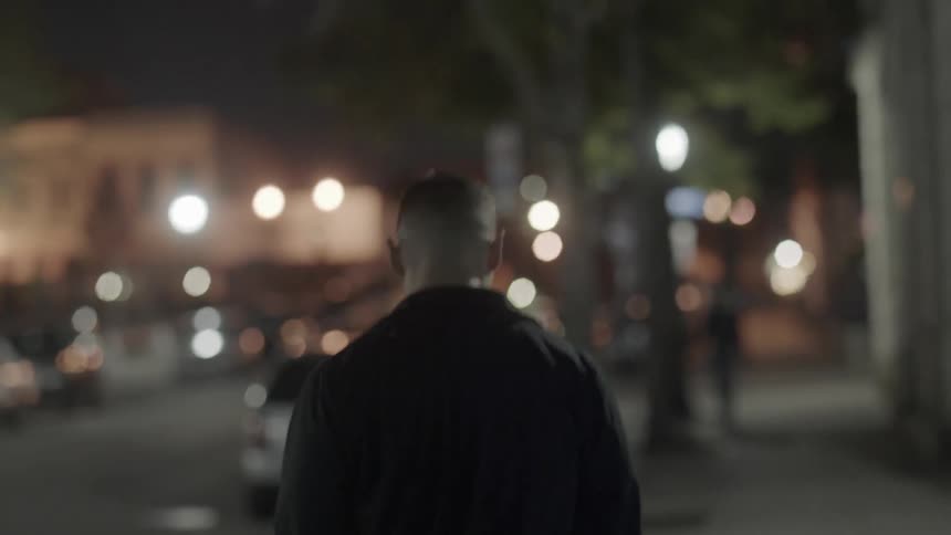 A man is walking down an urban street alone at night
