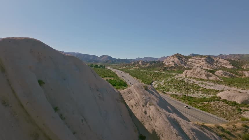 Cinematic aerial ascent over unique California desert rock formations reveals a highway with traffic below