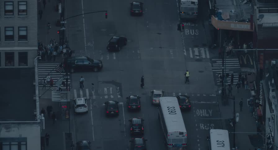 An aerial view of a busy city intersection at dusk shows cars, buses, and pedestrians moving through the streets