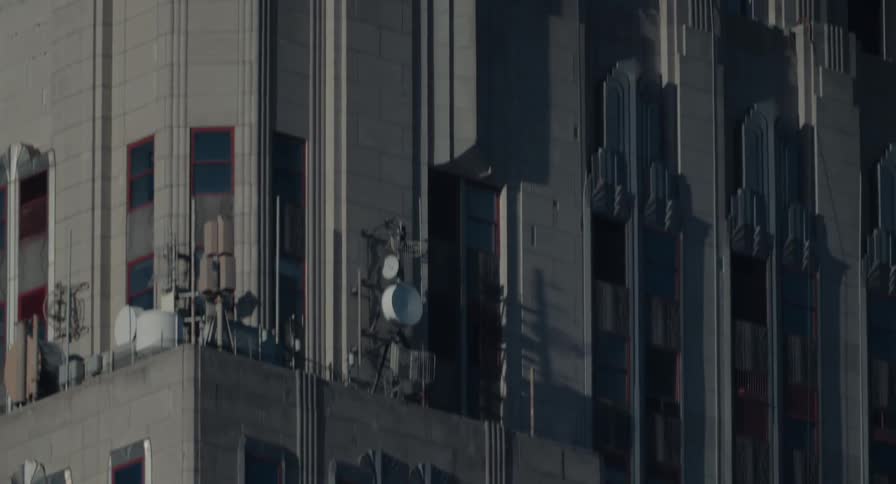 An extreme close-up telephoto shot slowly tilts up the iconic Empire State Building, revealing its Art Deco details and famous spire against a clear blue sky