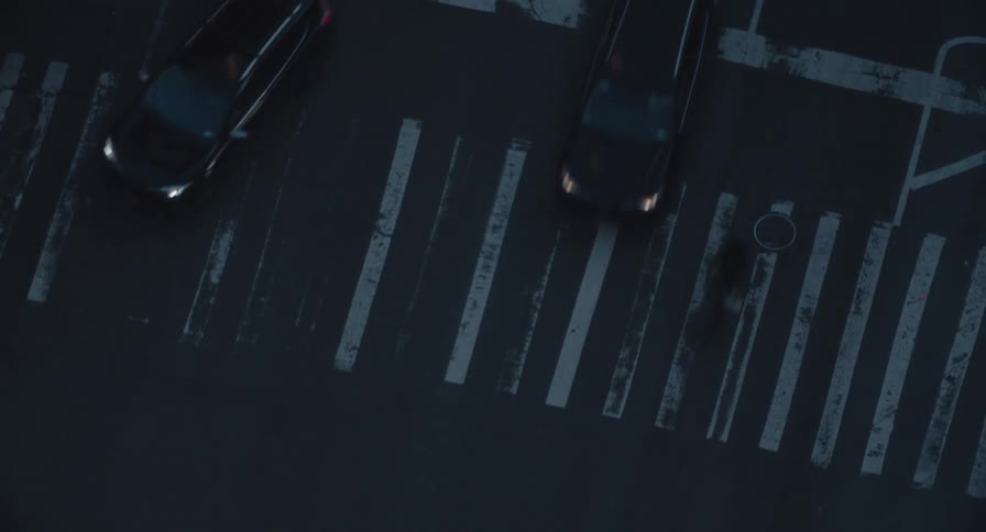Overhead view of cars and a yellow taxi driving through a crosswalk in the city at dusk