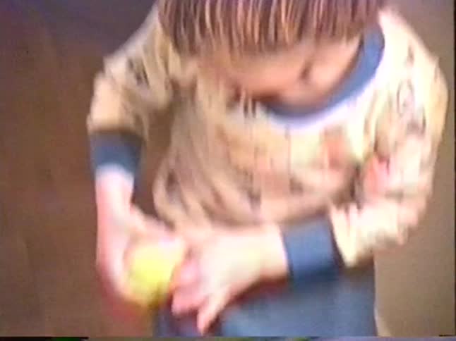 A nostalgic home video from the 1990s captures a young boy with a bowl cut playing with a ball in his pajamas
