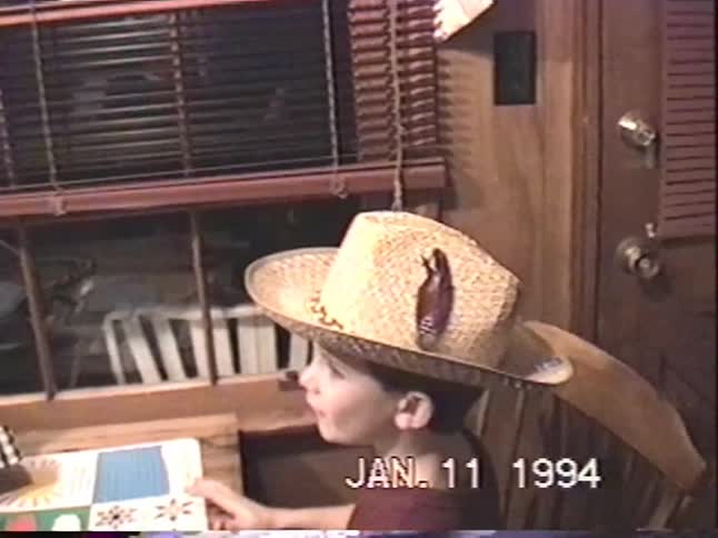 Candid 90s home video captures a young boy wearing a fun straw cowboy hat while sitting at the dinner table