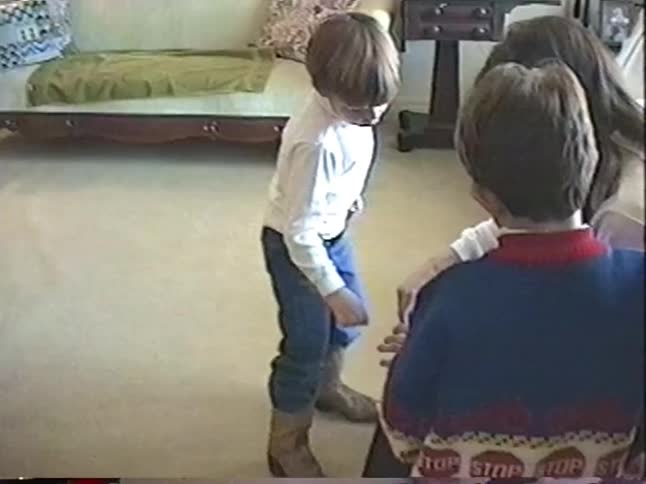 Two young boys watch as their mother unwraps a present in the living room in vintage footage