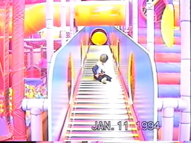 Vintage 1994 home video of a young boy sliding down a colorful roller slide at an indoor playground