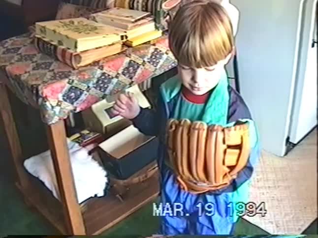 A nostalgic home video from 1994 shows a young boy with a bowl cut looking at his new baseball glove