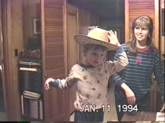 Vintage 1994 footage of a young boy playfully trying on an oversized straw hat with a woman in their home