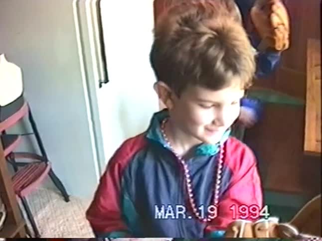 Two young boys in colorful 90s windbreakers show off their new baseball gloves in a home video from 1994