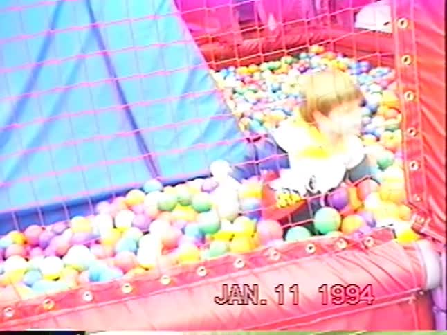 A happy young boy enjoys playing and wading through a sea of colorful balls in a ball pit in this vintage home video from 1994